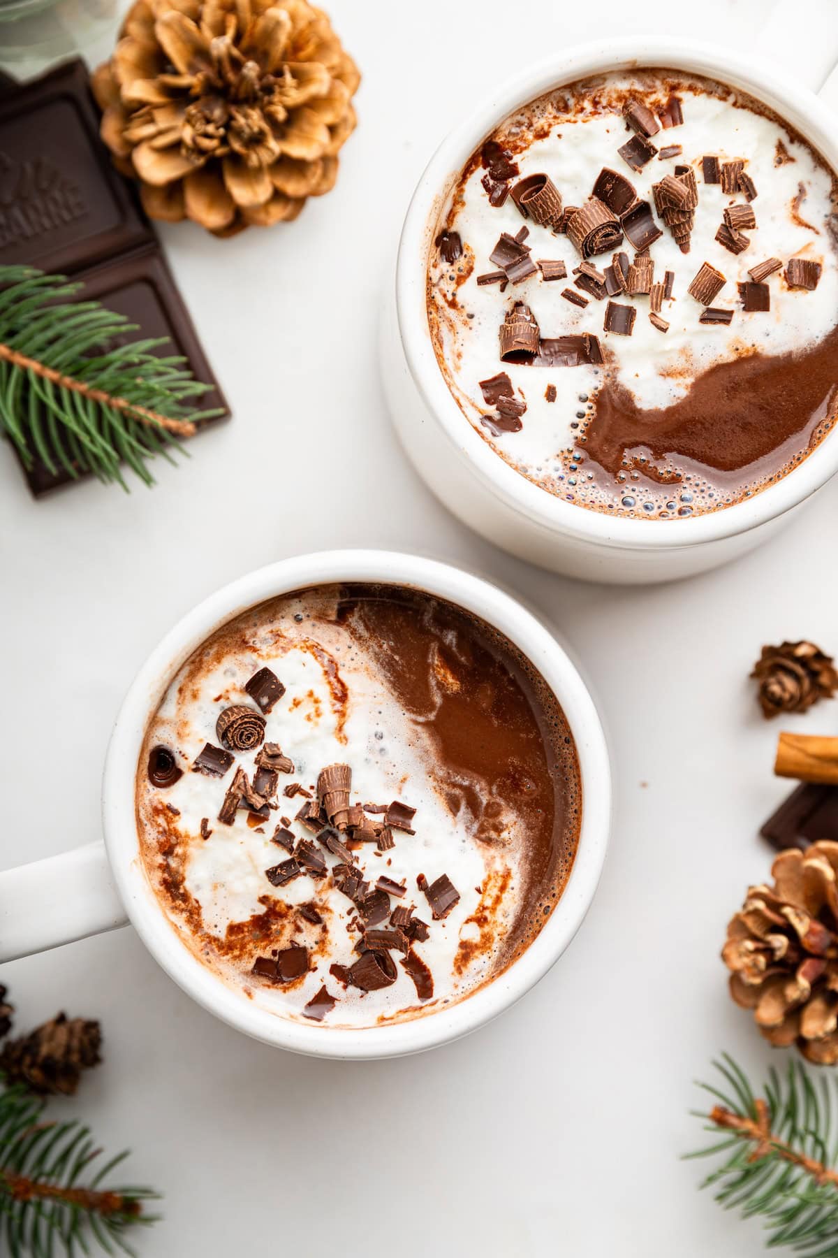 Two white mugs of hot chocolate topped with a little whip cream and chocolate shavings.
