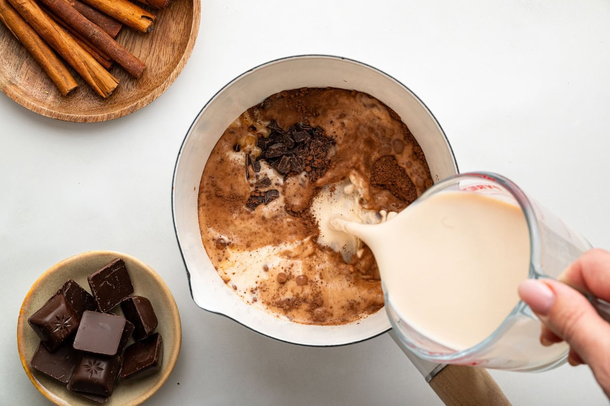 A woman's hand pouring milk into a saucepan with the rest of the hot chocolate ingredients.