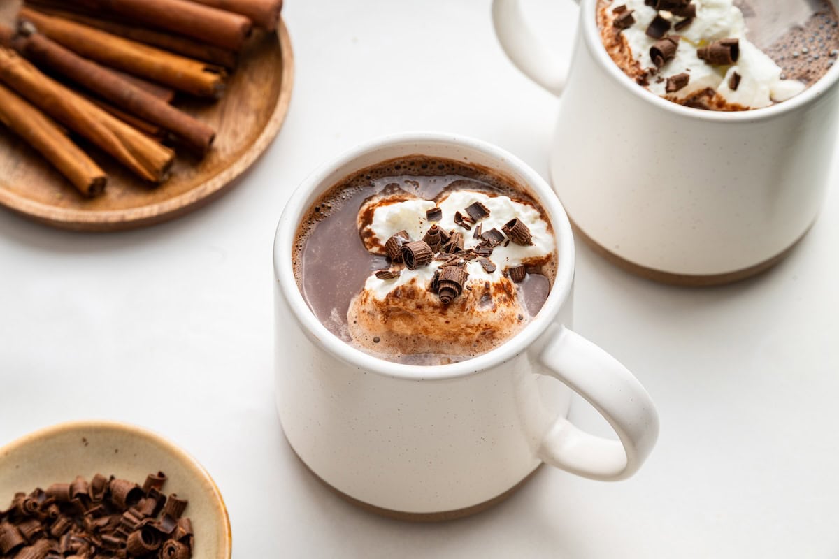 Two white mugs of hot chocolate topped with a little whip cream and chocolate shavings.
