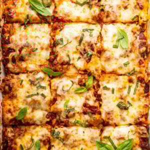 Healthy lasagna in a baking dish, cut into squares, and garnished with fresh basil and parsley.