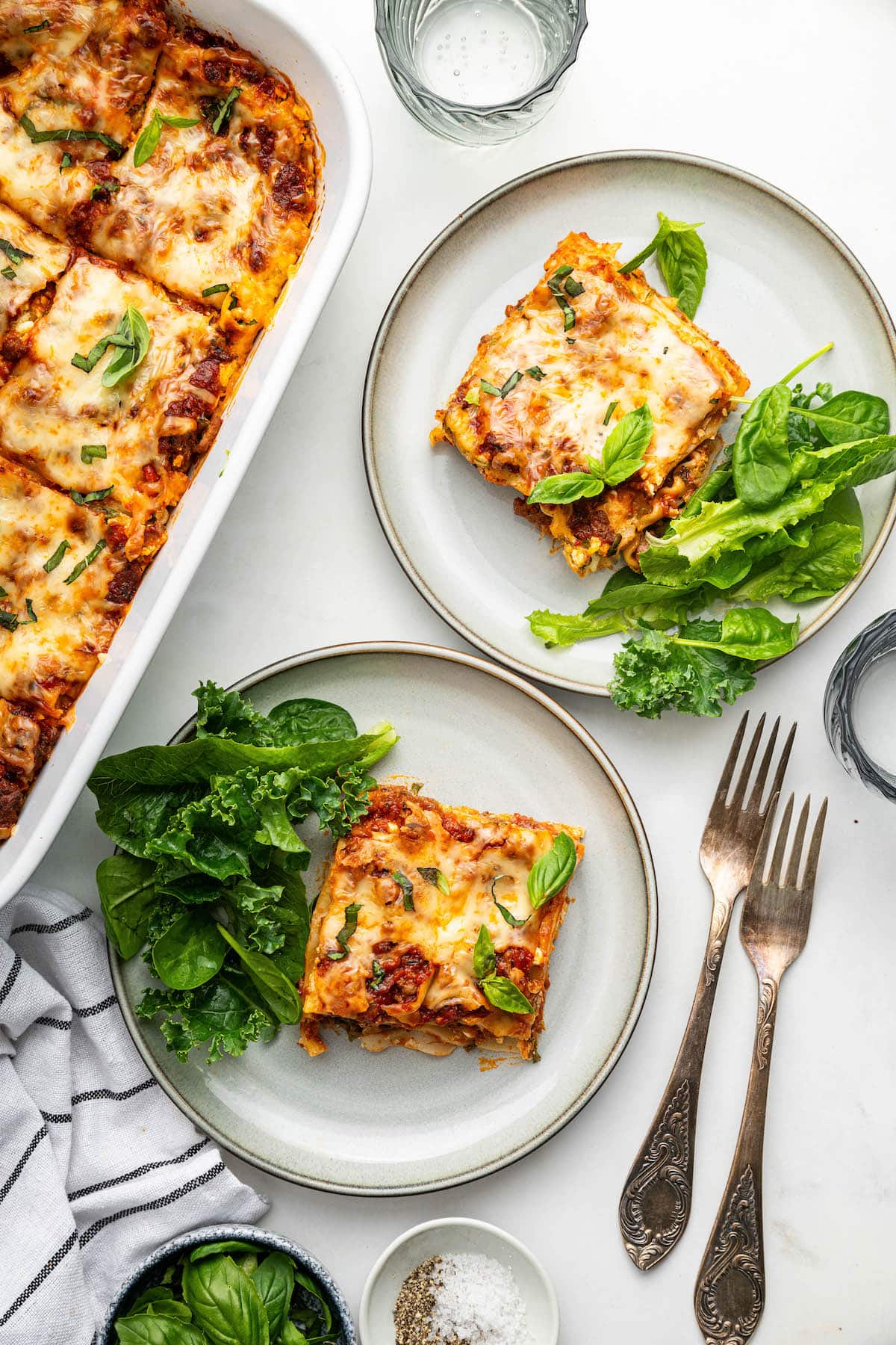 Two plates of healthy lasagna with side salads on each plate.