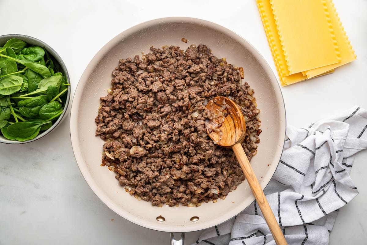 A skillet with cooked ground beef and a wooden spoon.