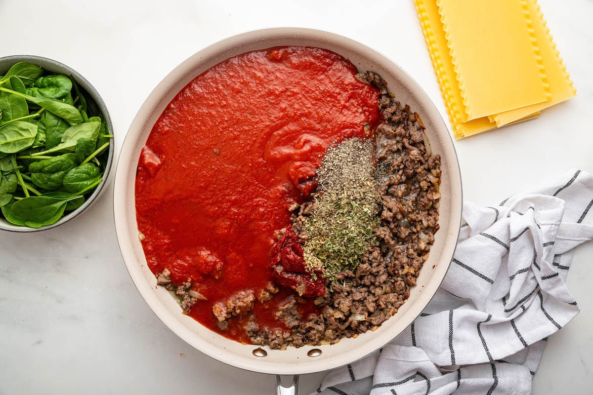 A skillet with cooked ground beef with tomato sauce and dried herbs.