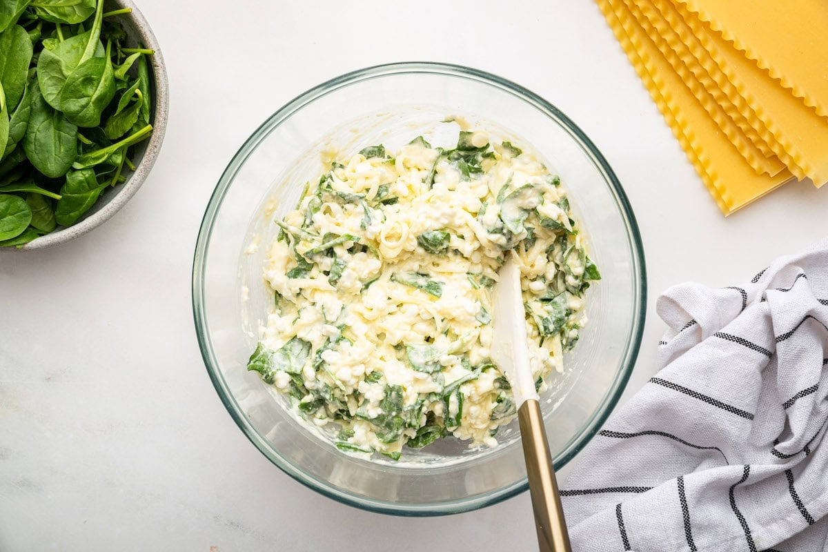 A large glass bowl of multiple cheeses, spinach, and garlic that will be used for a healthy lasagna.