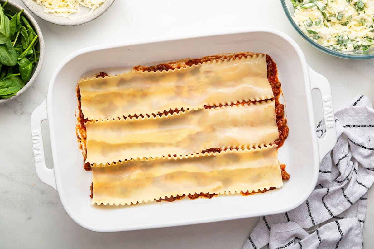A baking dish of a healthy lasagna being prepared with a base of tomato sauce and lasagna noodles on top.