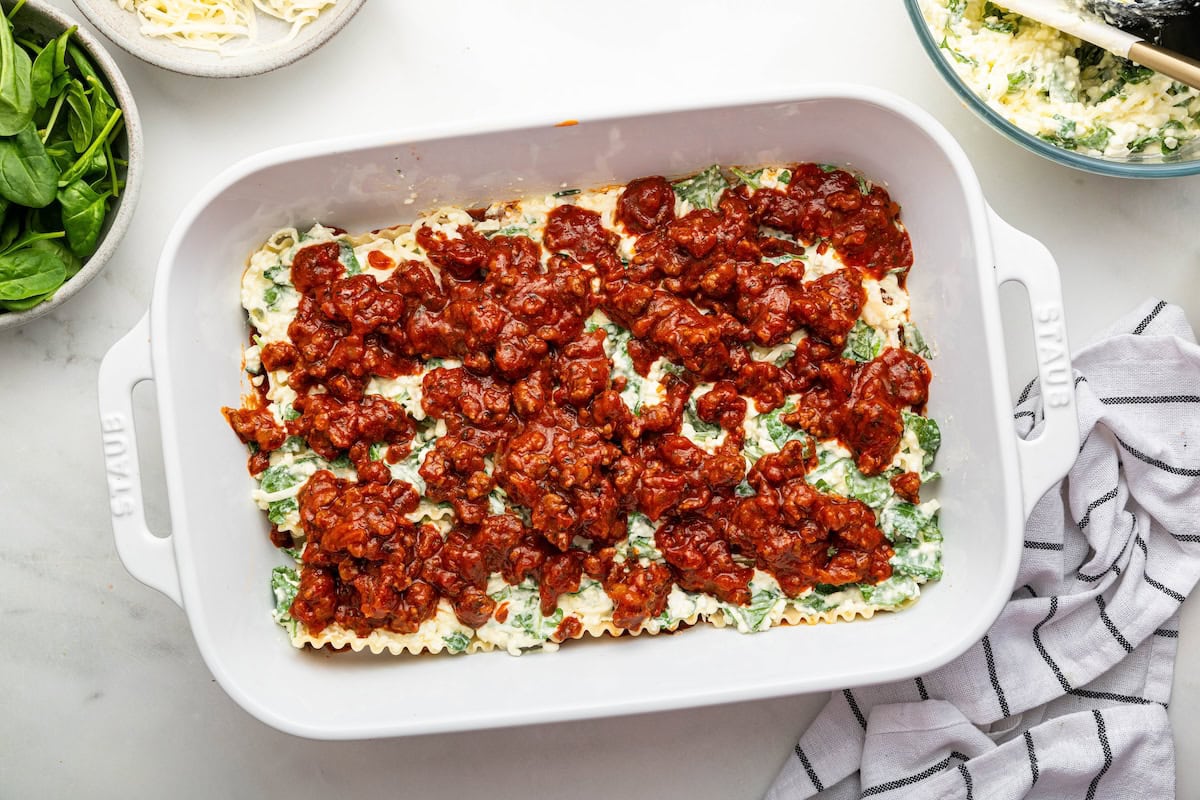 A layer of tomato sauce over a cheese layer in a baking dish for healthy lasagna.