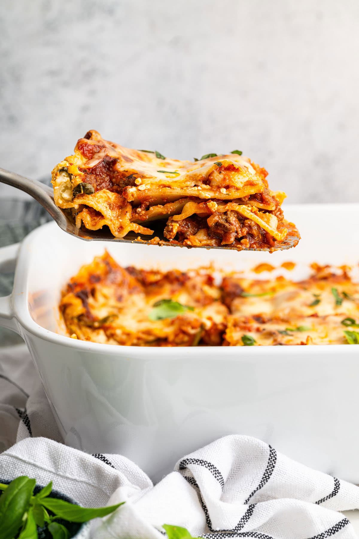 A serving of healthy lasagna being lifted by a spatula from a baking dish.