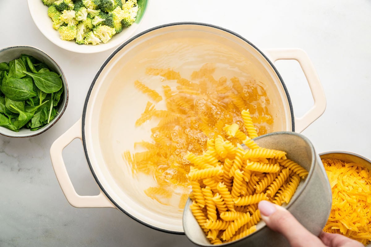 A woman's hand dumping rotini pasta into a pot of boiling water.