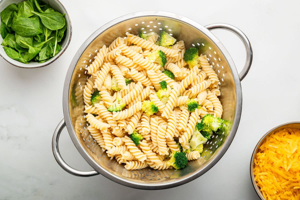The rotini pasta and broccoli florets in a silver colander after being drained.