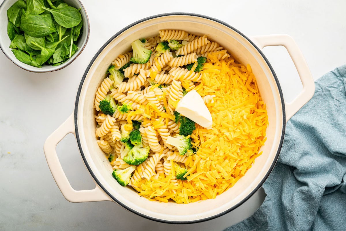 The rotini pasta, broccoli, shredded cheddar cheese and laughing cow cheese wedge in a pot.