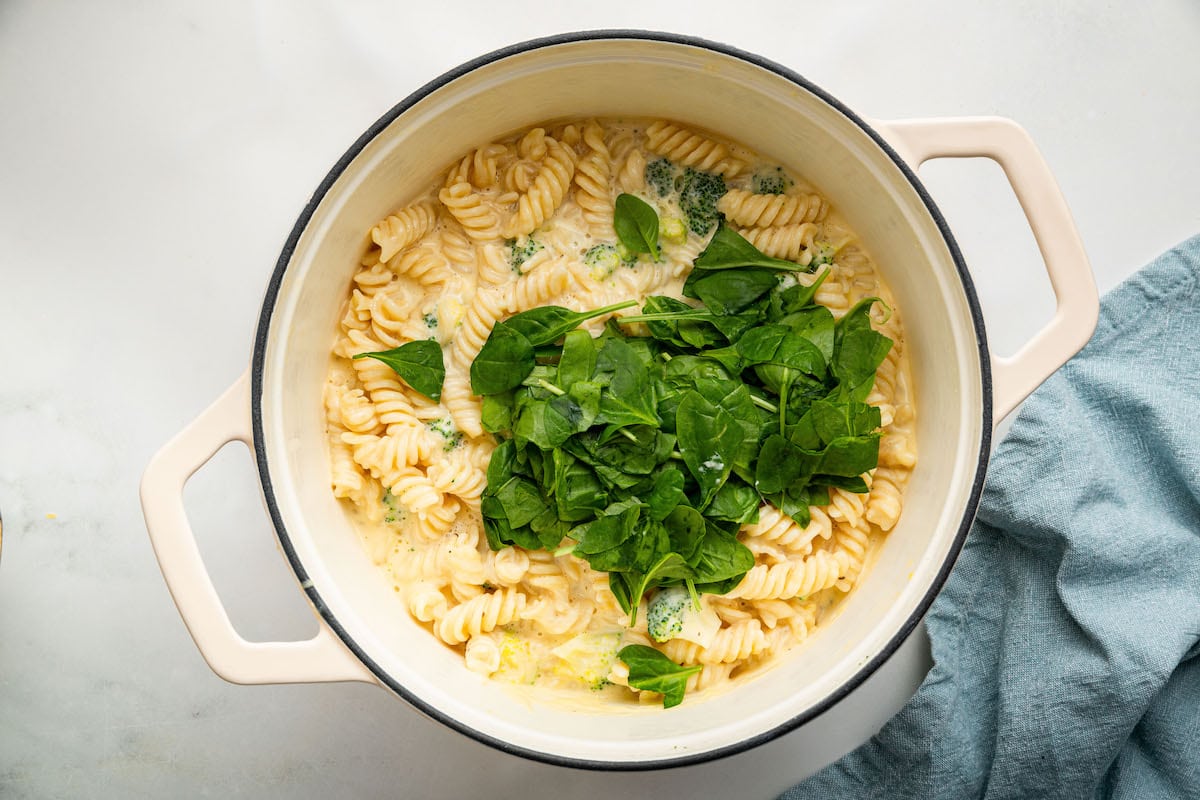 Spinach added to the rotini pasta and broccoli florets in a simmering cheese sauce.