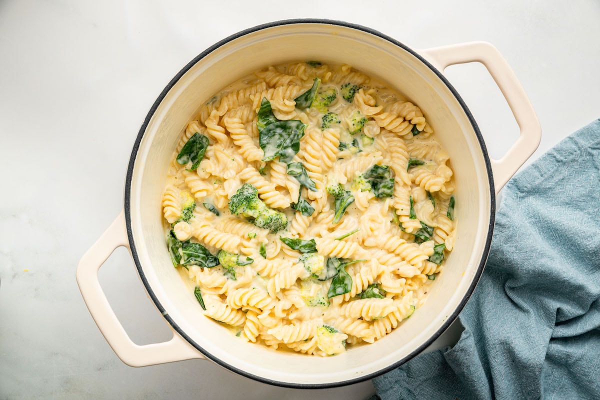 Rotini pasta, broccoli and spinach in a pot coated in a cheese sauce.