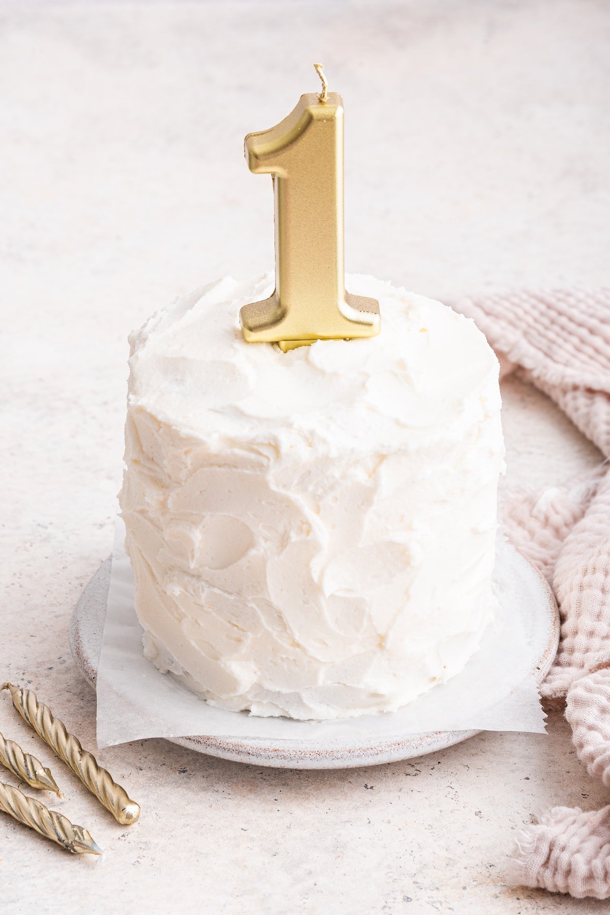 A frosted smash cake with a one candle on top.