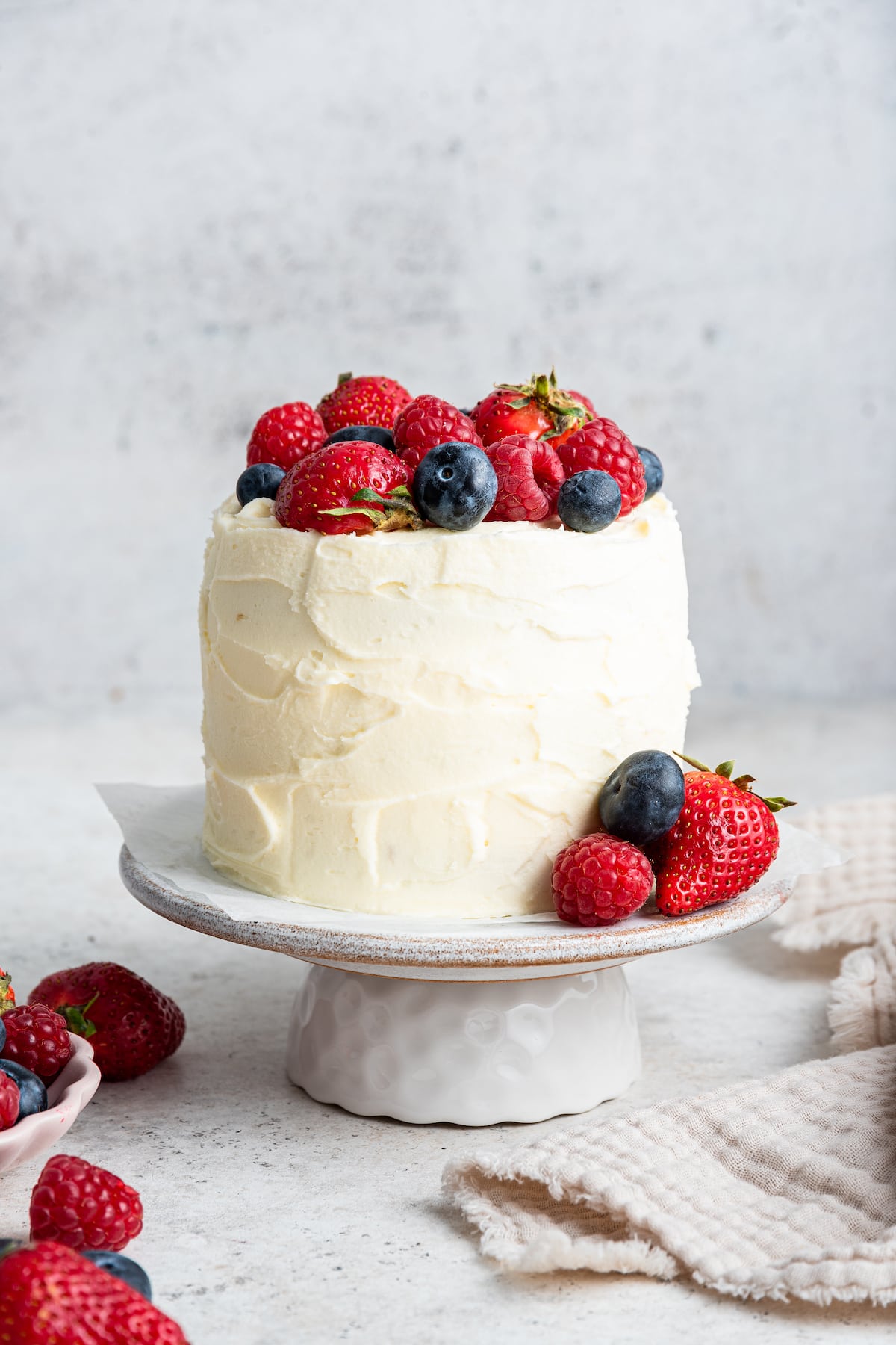 A frosted smash cake topped with fresh berries sitting on a cake stand.