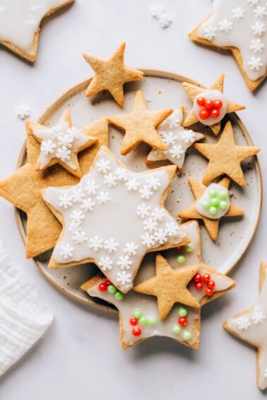 An overhead photo looking at a plate of healthy sugar cookies. Some of the cookies have been decorated with white icing and red, green or white sprinkles and some of the cookies are plain.