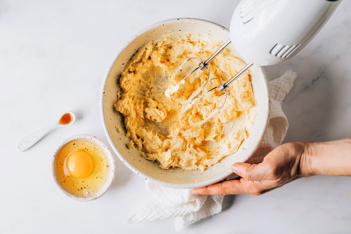 A hand mixer is blending together butter and maple syrup.