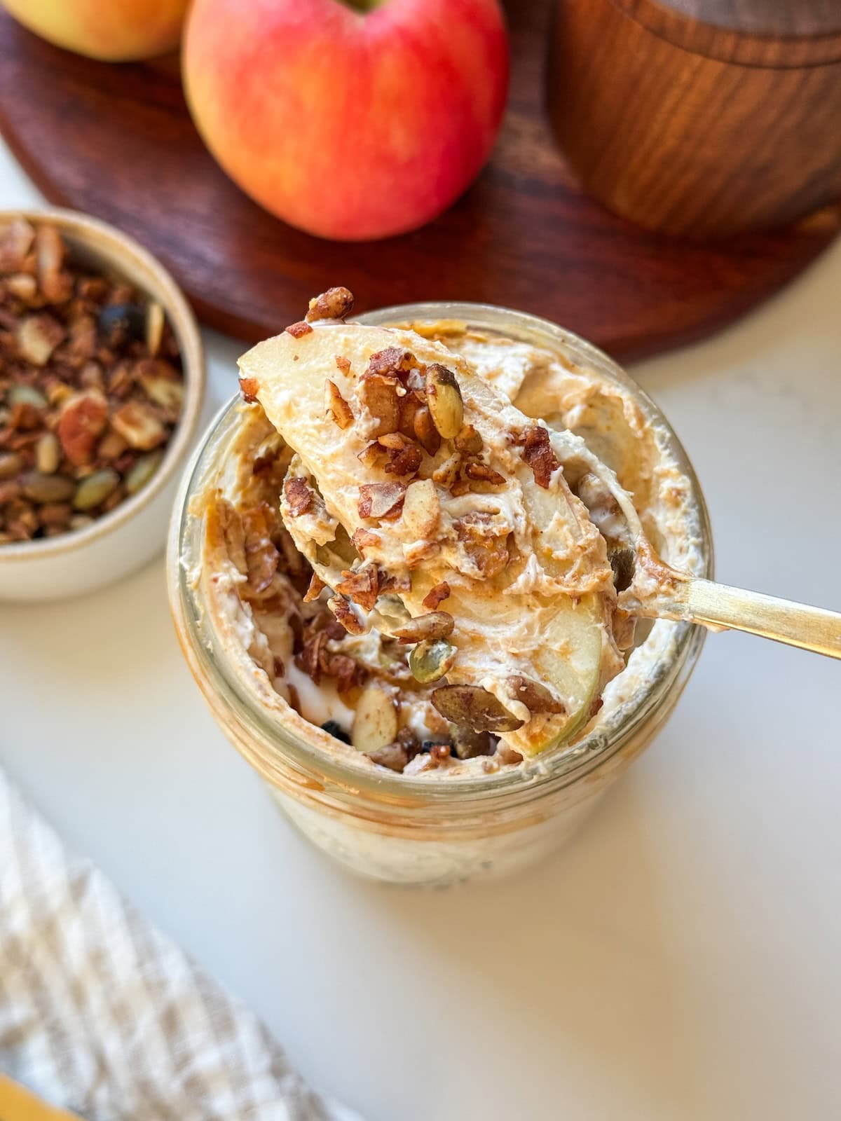 A spoonful of high protein apple salad with an apple slice and granola, held over a mason jar.