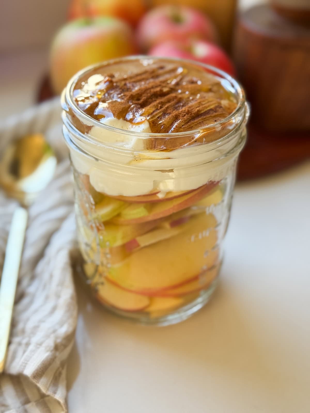 A glass mason jar layered with apple slices, yogurt, peanut butter, and cinnamon with a drizzle of honey at the top.