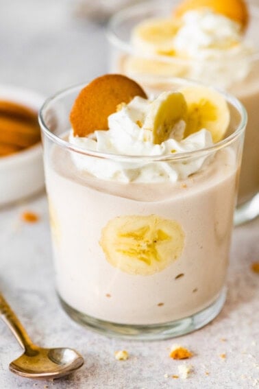 High-protein banana pudding in a glass topped with whipped cream, sliced bananas and a wafer cookie.