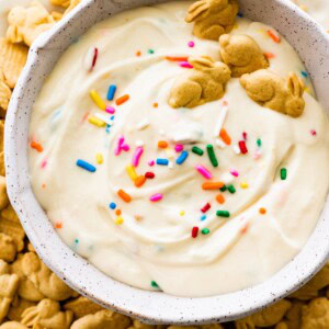 Protein Dunkaroo dip in a white bowl with four bunny crackers in the dip and more bunny crackers on the side.
