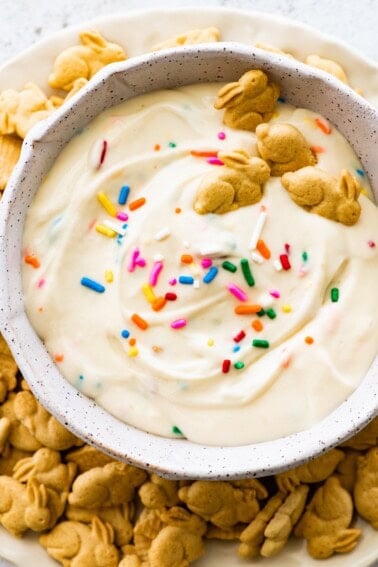 Protein Dunkaroo dip in a white bowl with four bunny crackers in the dip and more bunny crackers on the side.