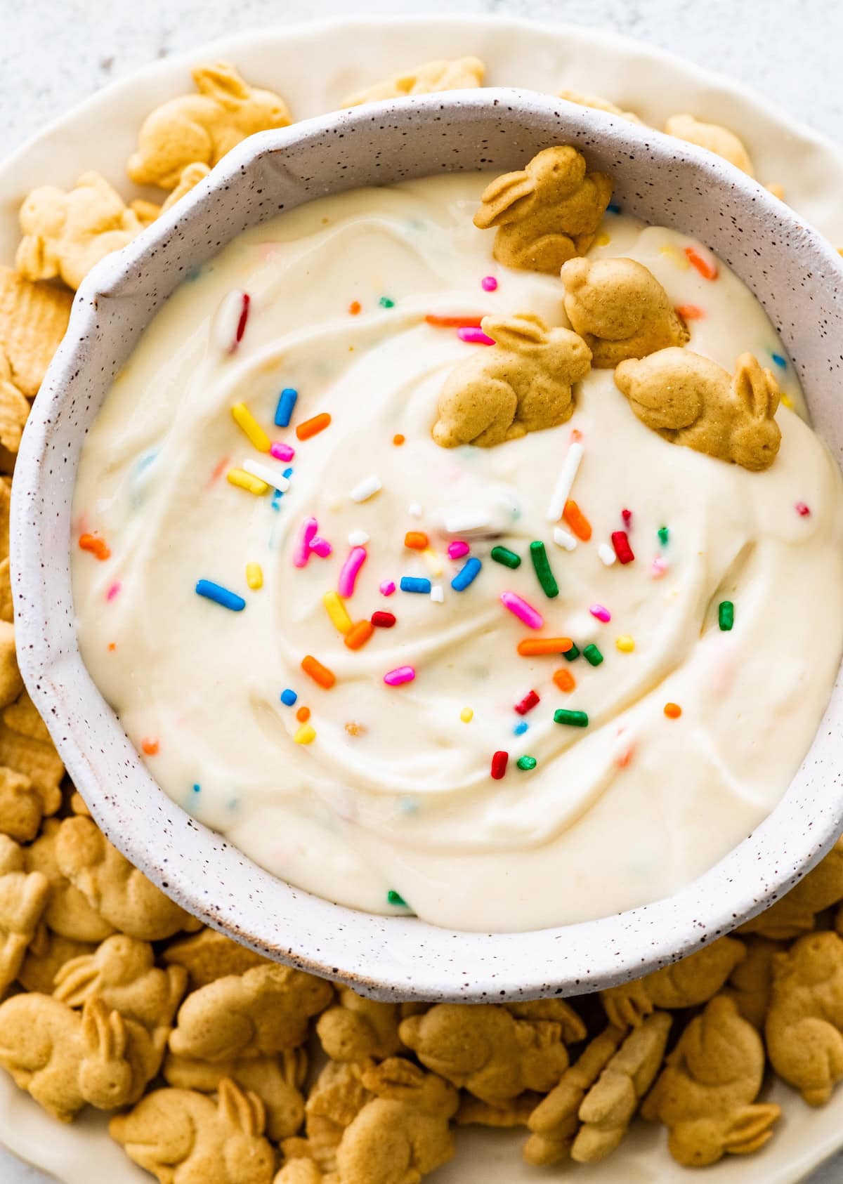 Protein Dunkaroo dip in a white bowl with four bunny crackers in the dip and more bunny crackers on the side.