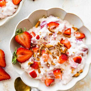 A bowl of strawberry pretzel salad topped with strawberries and crushed pretzels.