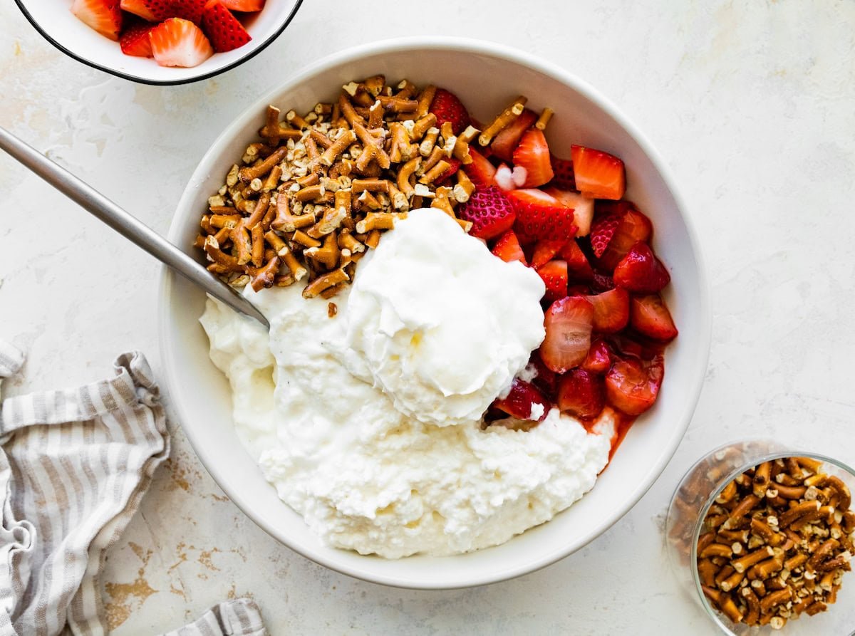 A bowl with cottage cheese, yogurt, chopped strawberries, and crushed pretzels before mixing.