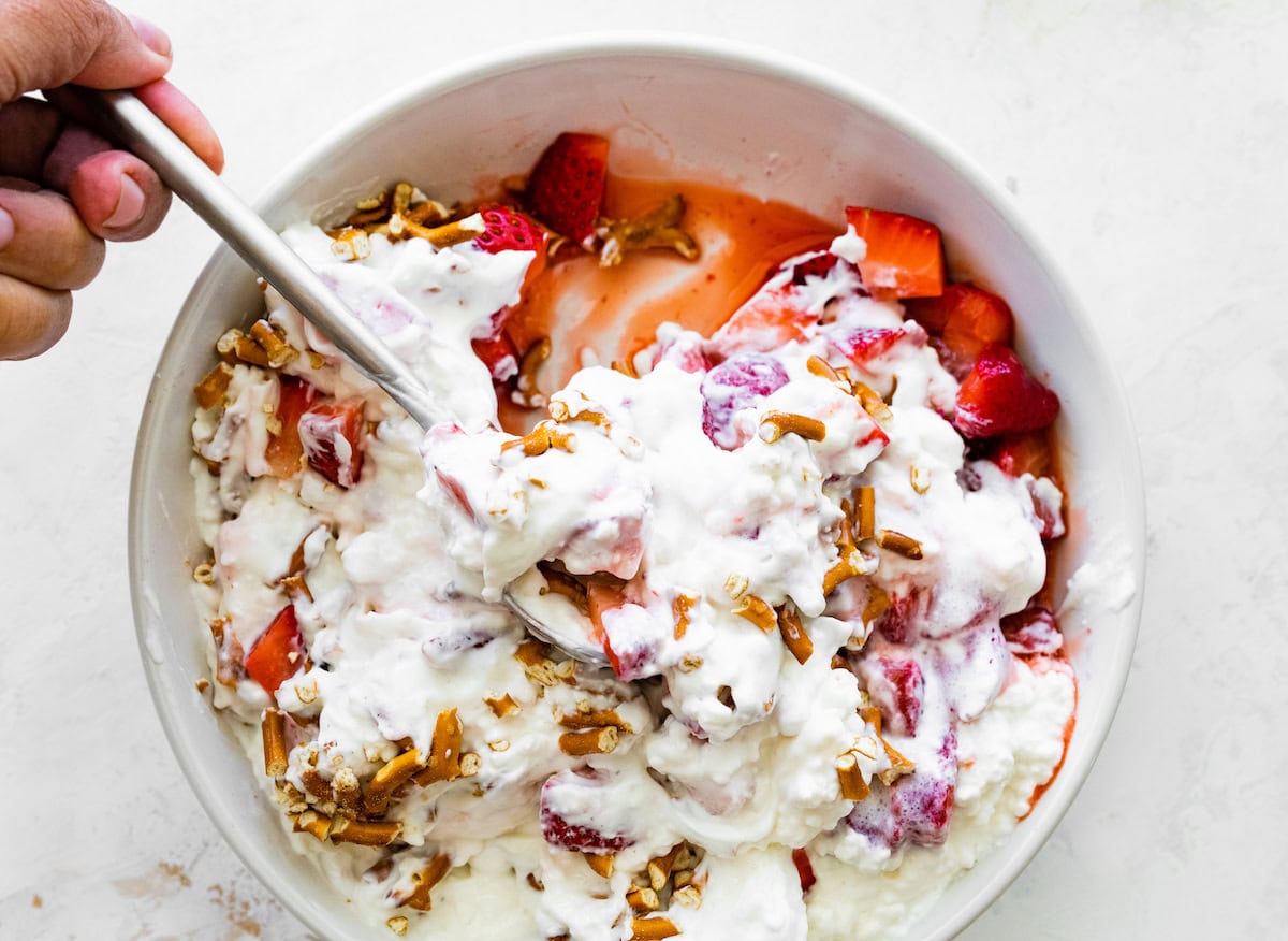 Strawberry pretzel salad being stirred together in a white bowl.