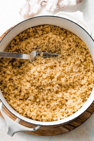 A large white pot filled with cooked quinoa. There is a silver fork in the quinoa.