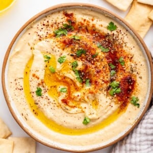 A bowl of creamy hummus topped with olive oil, herbs, and spices.