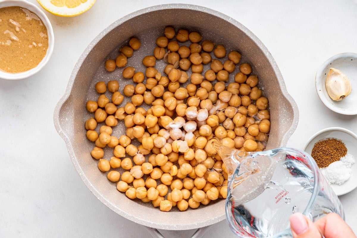 A woman's hand pours water in a large pot of garbanzo beans.
