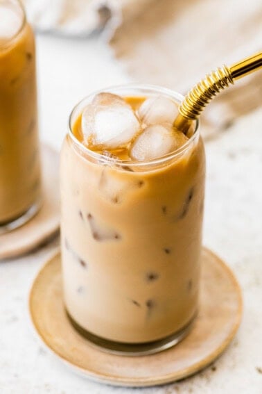 Finished iced coffee with a creamy light brown color and ice cubes, served with a gold metal straw.