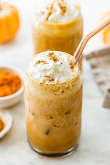 Two iced pumpkin spice lattes with whipped cream and straw.