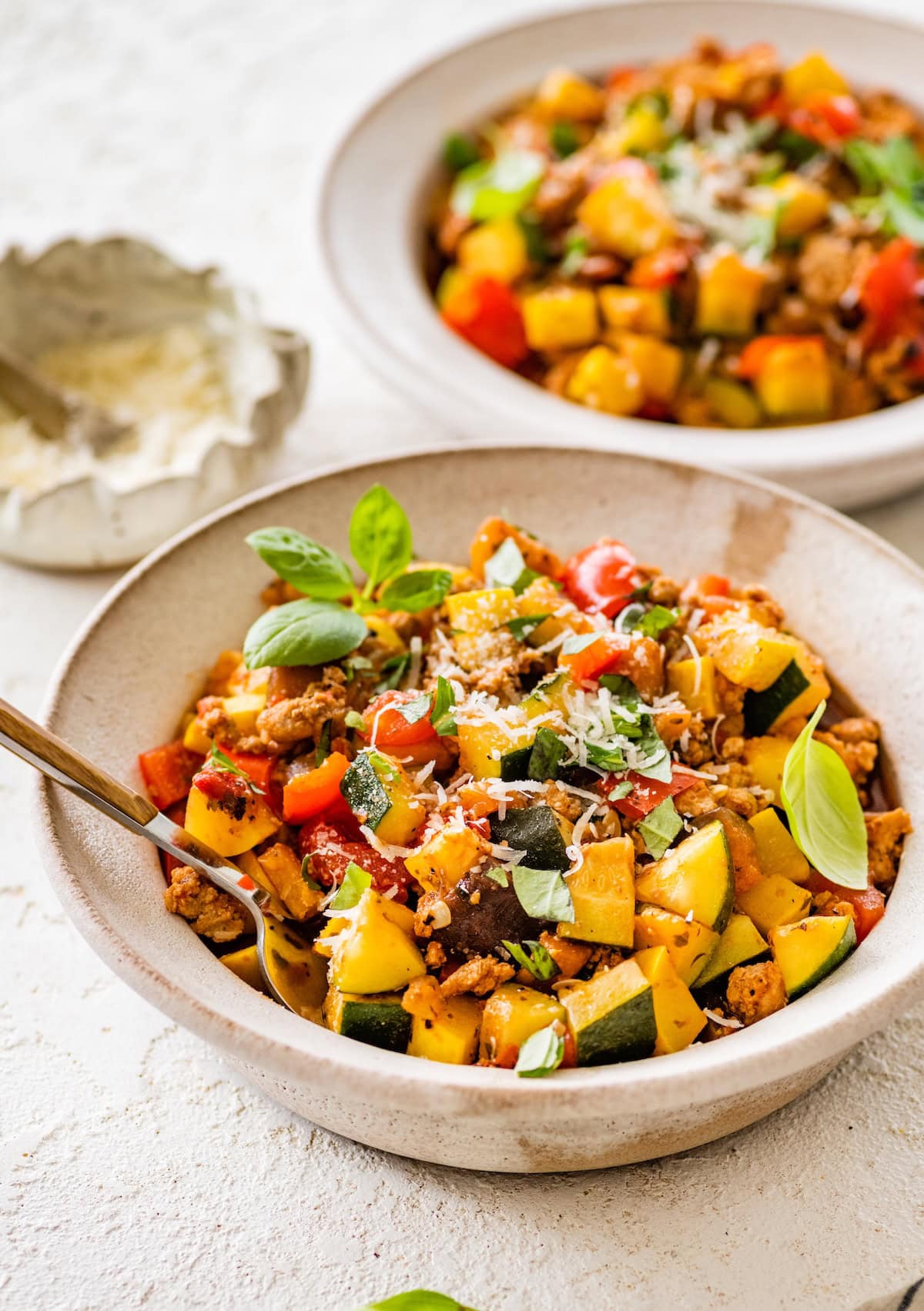 Two bowls of Italian ground turkey and veggie skillet garnished with basil and parmesan.