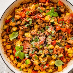 Large skillet filled with cooked ground turkey, vegetables, and tomato sauce topped with basil.
