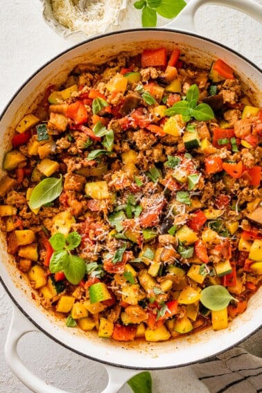 Large skillet filled with cooked ground turkey, vegetables, and tomato sauce topped with basil.