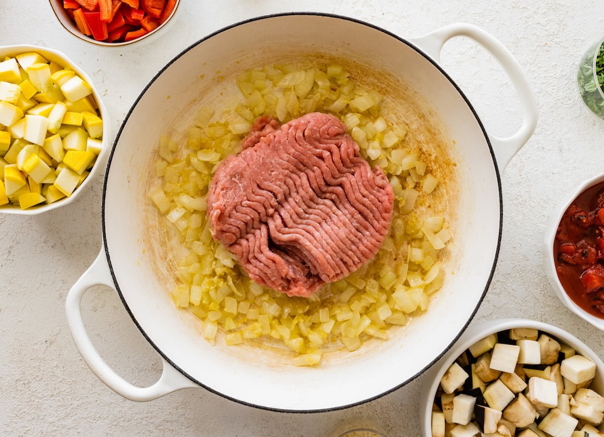 Raw ground turkey cooking with sautéed onions and garlic in a large skillet.