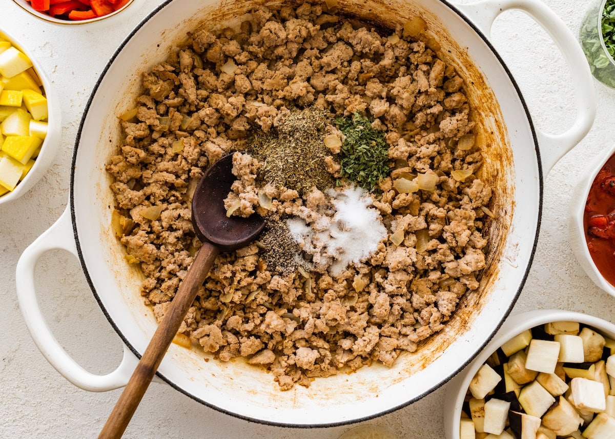 Ground turkey in a skillet seasoned with dried herbs, salt, and pepper.