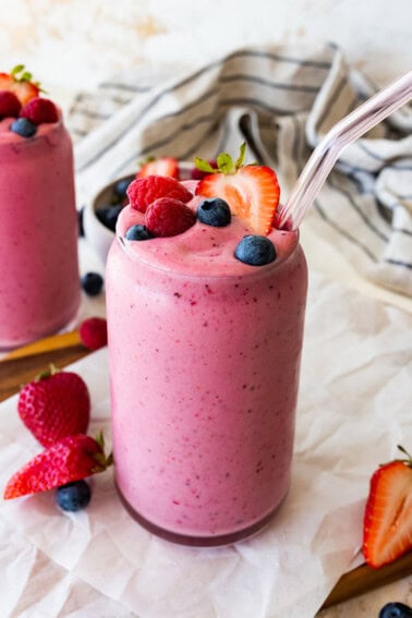 Two glasses filled with the berry kefir smoothie topped with fresh blueberries, raspberries and strawberries.