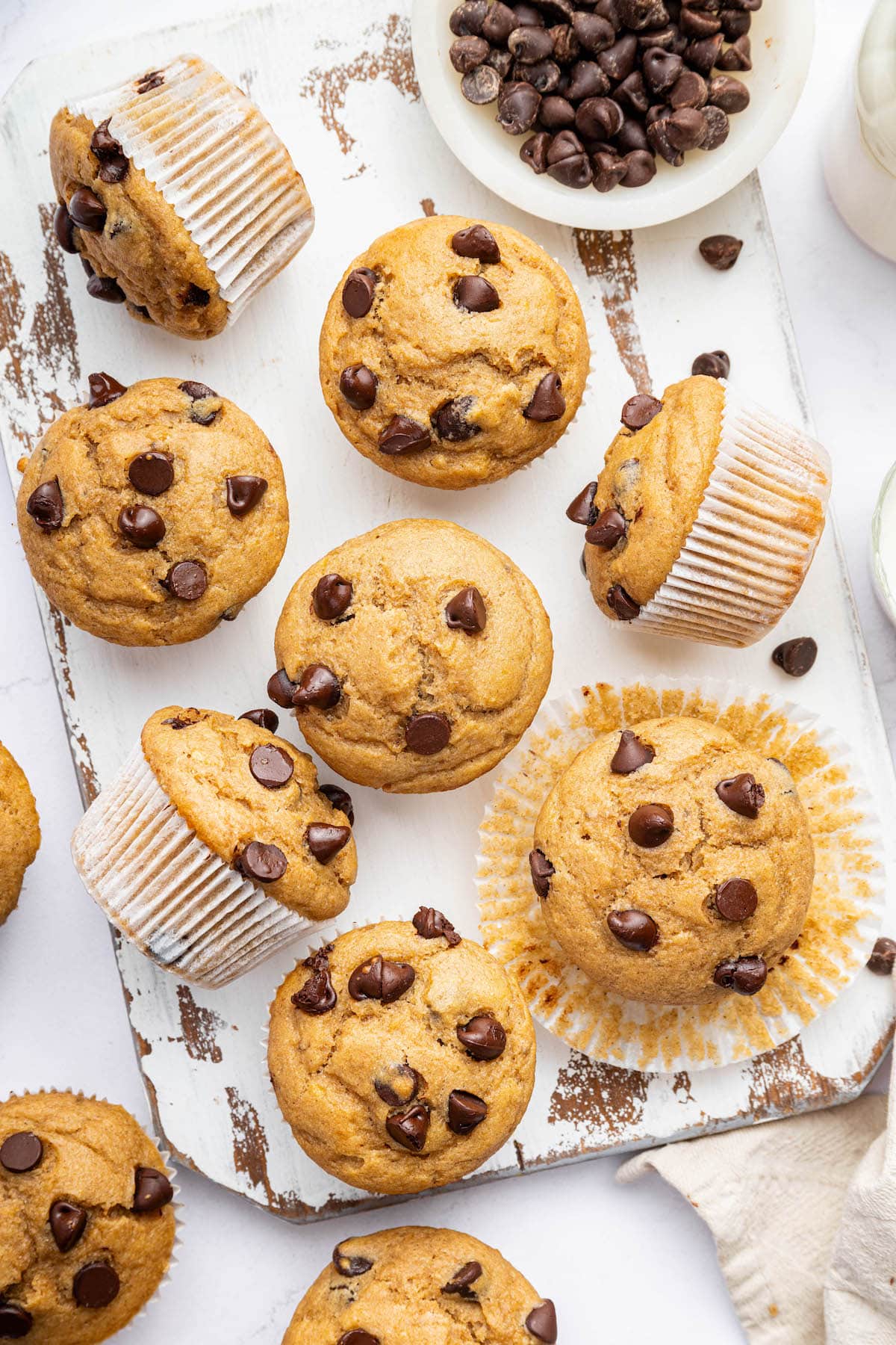 Several Kodiak cake muffins on a wooden board, with chocolate chips scattered around.