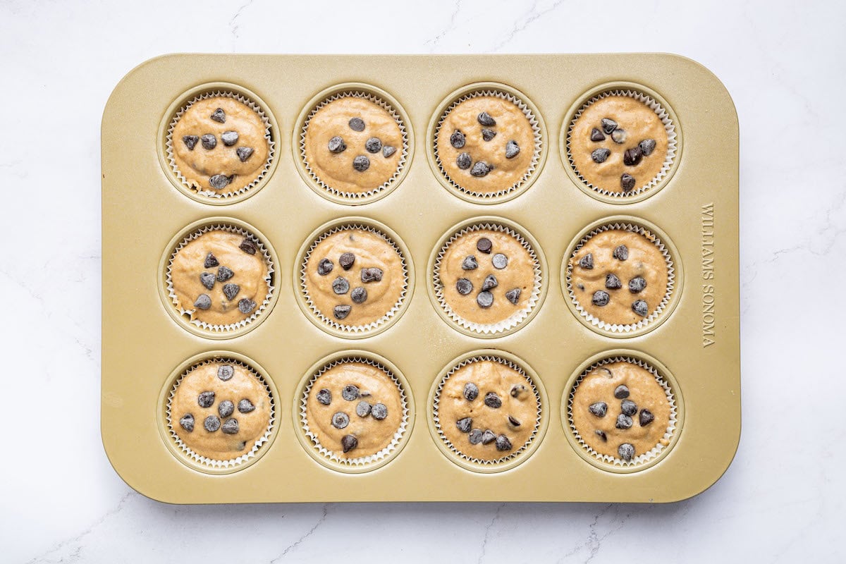 A muffin tin filled with Kodiak cake muffin batter, each cup sprinkled with chocolate chips before baking.