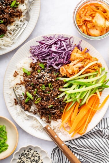 Korean beef served over white rice with fresh carrots, purple cabbage, cucumber and kimchi. The beef is topped with sesame seeds and green onions.