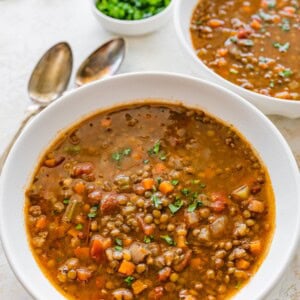 A white bowl of lentil soup with roasted garlic and vegetables.