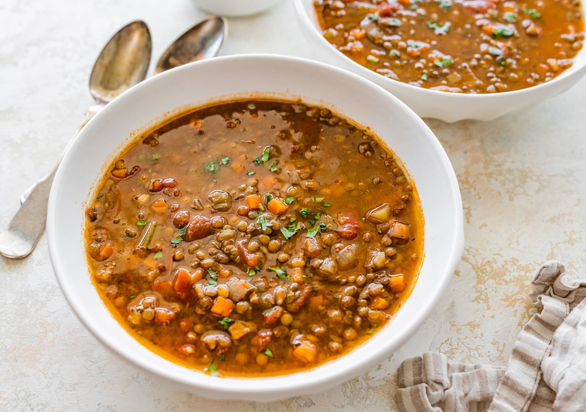 A white bowl of lentil soup with roasted garlic and vegetables.