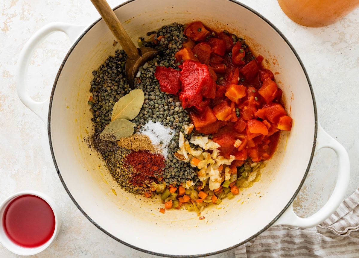 A large pot with sauteed onion, carrot, and celery with diced tomato, tomato paste, lentils, herbs, and spices.