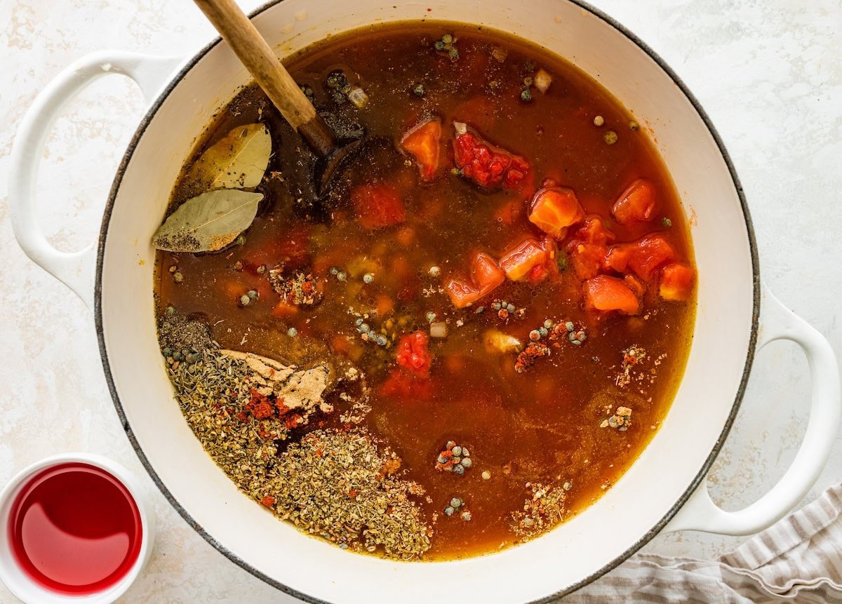 A large pot of lentil soup before being cooked with a large wooden serving spoon.