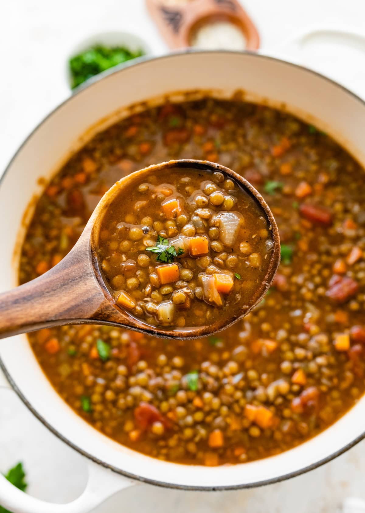 A wooden spoon with lentil soup over a large pot of the soup.