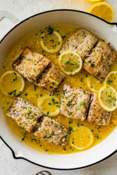4 Mahi mahi fillets in a skillet with a lemon butter garlic sauce. There are lemon slices in the skillet and everything is topped with fresh parsley.
