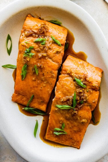 Two maple glazed salmon filets on a plate topped with green onion.